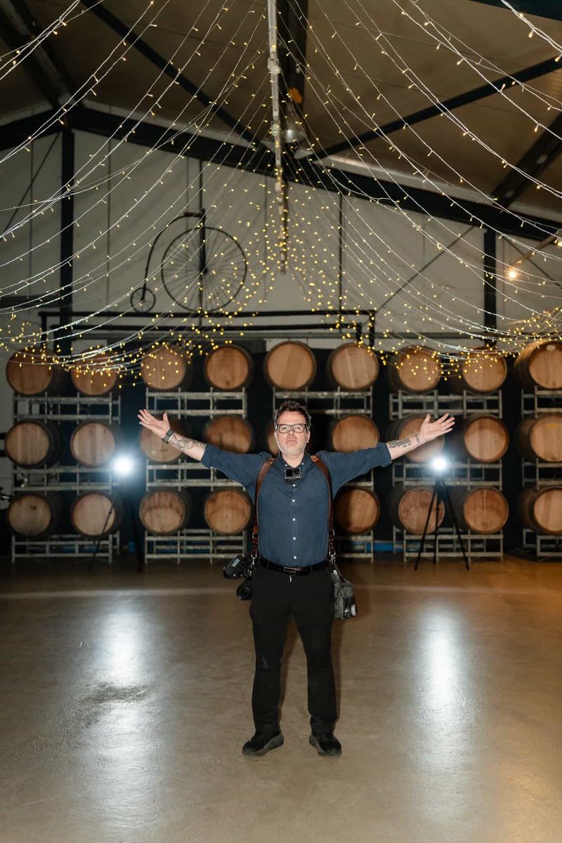 Gareth, arms wide, in a barrel room strung with fairy lights